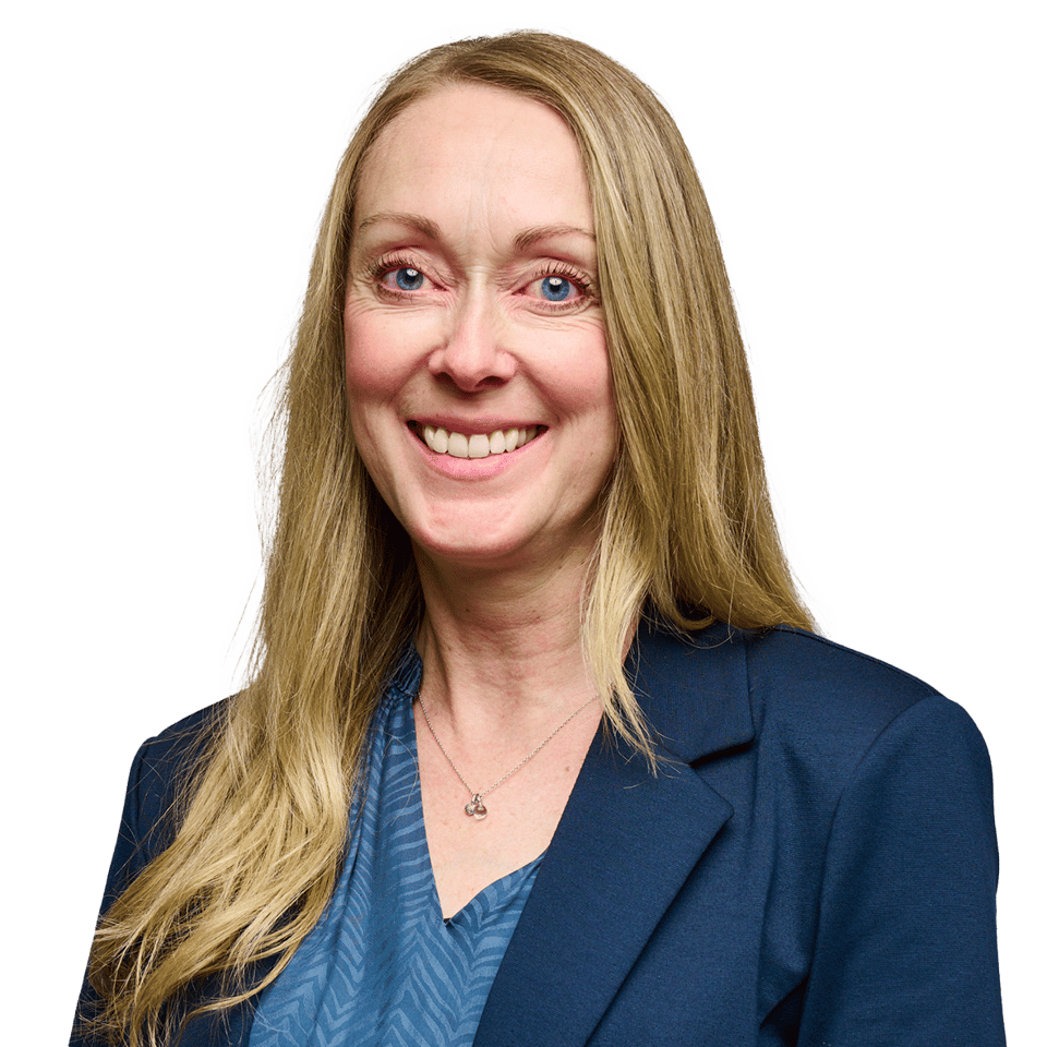 Portræt af en smilende kvinde med langt lyst hår og blå øjne, iført en mørkeblå blazer og en mønstret blå bluse.